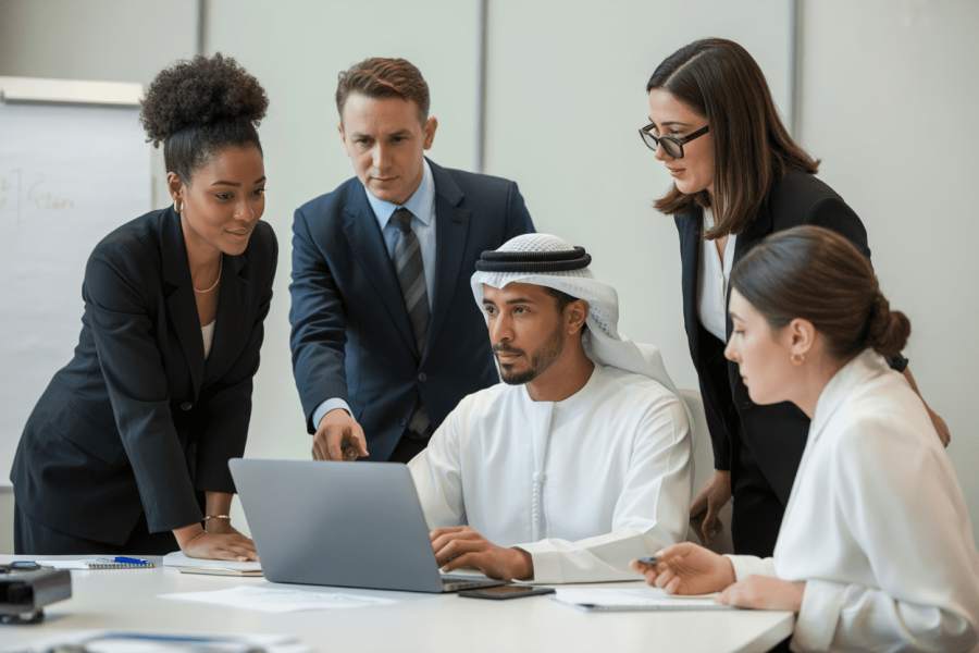 A diverse group of professionals collaborates around a laptop in a modern conference room, discussing ideas and strategies.